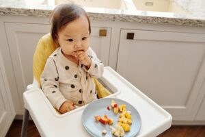 Baby self-feeding cut pieces of fruit during baby-led weaning in a high chair