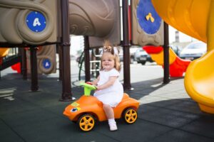 Toddler girl playing on a ride-on toy car outdoors in a sunny backyard