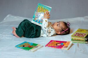 Toddler lying down reading a stack of children's books
