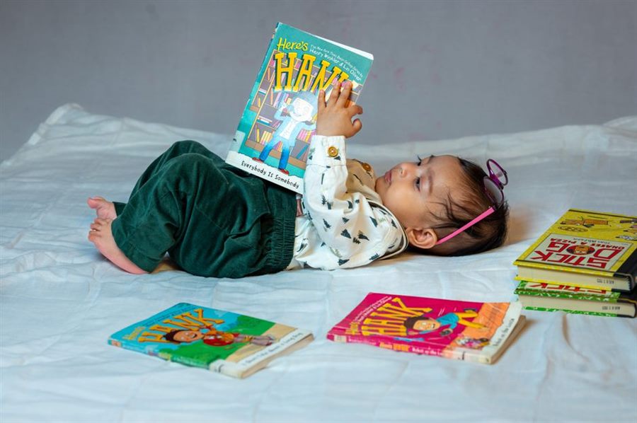 Toddler lying down reading a stack of children's books