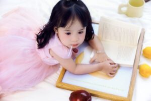 Toddler girl sitting on the floor reading a picture book, browsing books for toddler girls