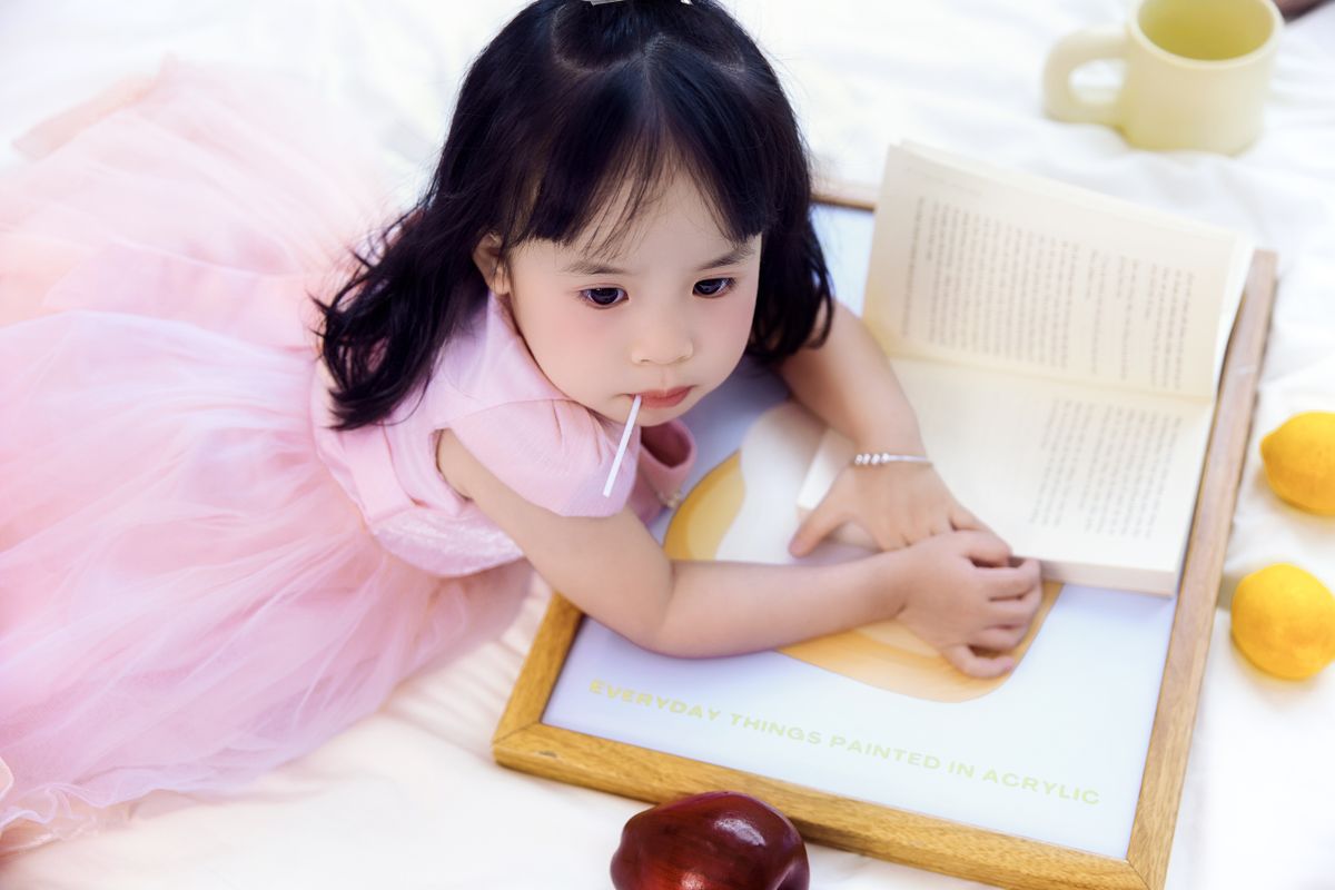 Toddler girl sitting on the floor reading a picture book, browsing books for toddler girls