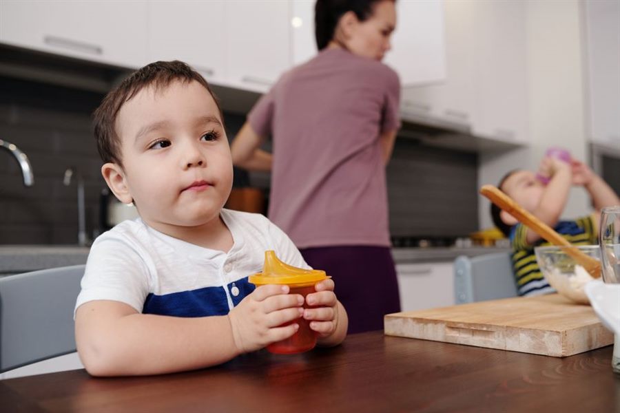 Toddler holding an orange sippy cup at the kitchen table
