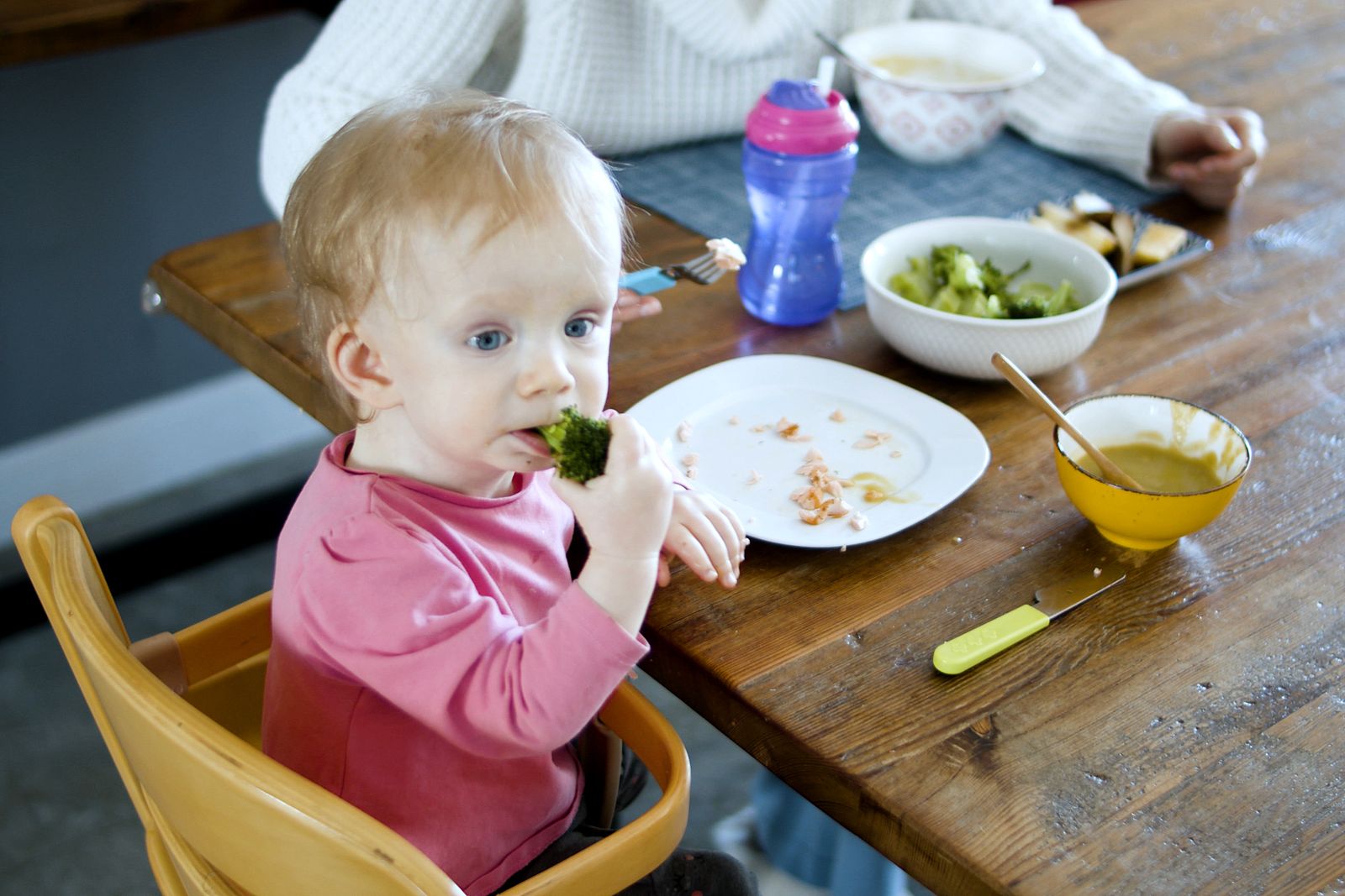 Lunch ideas for toddlers: toddler in a high chair eating broccoli and rice from a divided tray