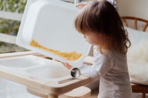 Sensory activities for toddlers: toddler pouring pasta in a sensory tray