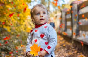 Thanksgiving activities for toddlers: toddler holding a maple leaf outdoors