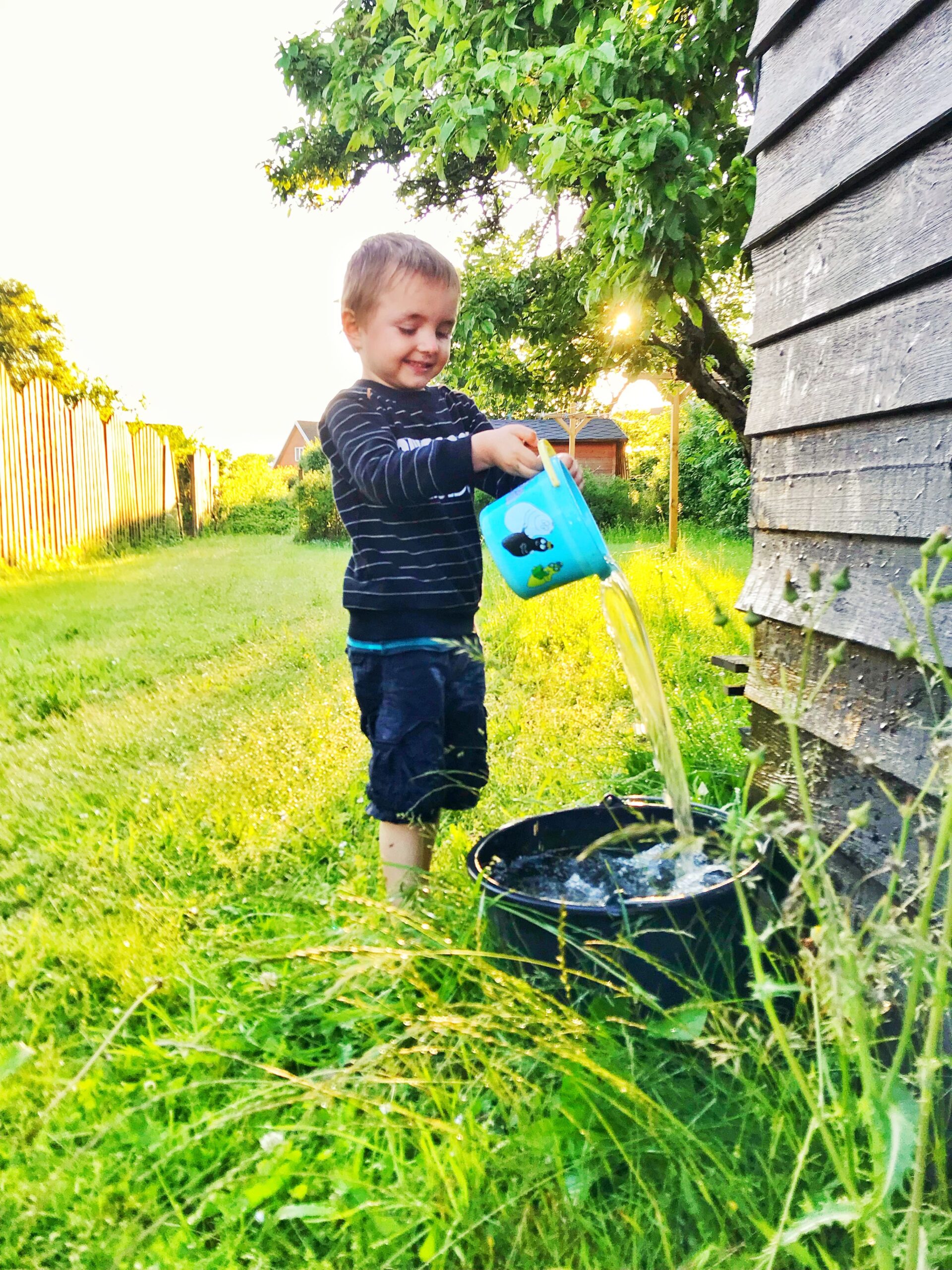 Toddler playing outdoors with a watering can, an outdoor sensory activity