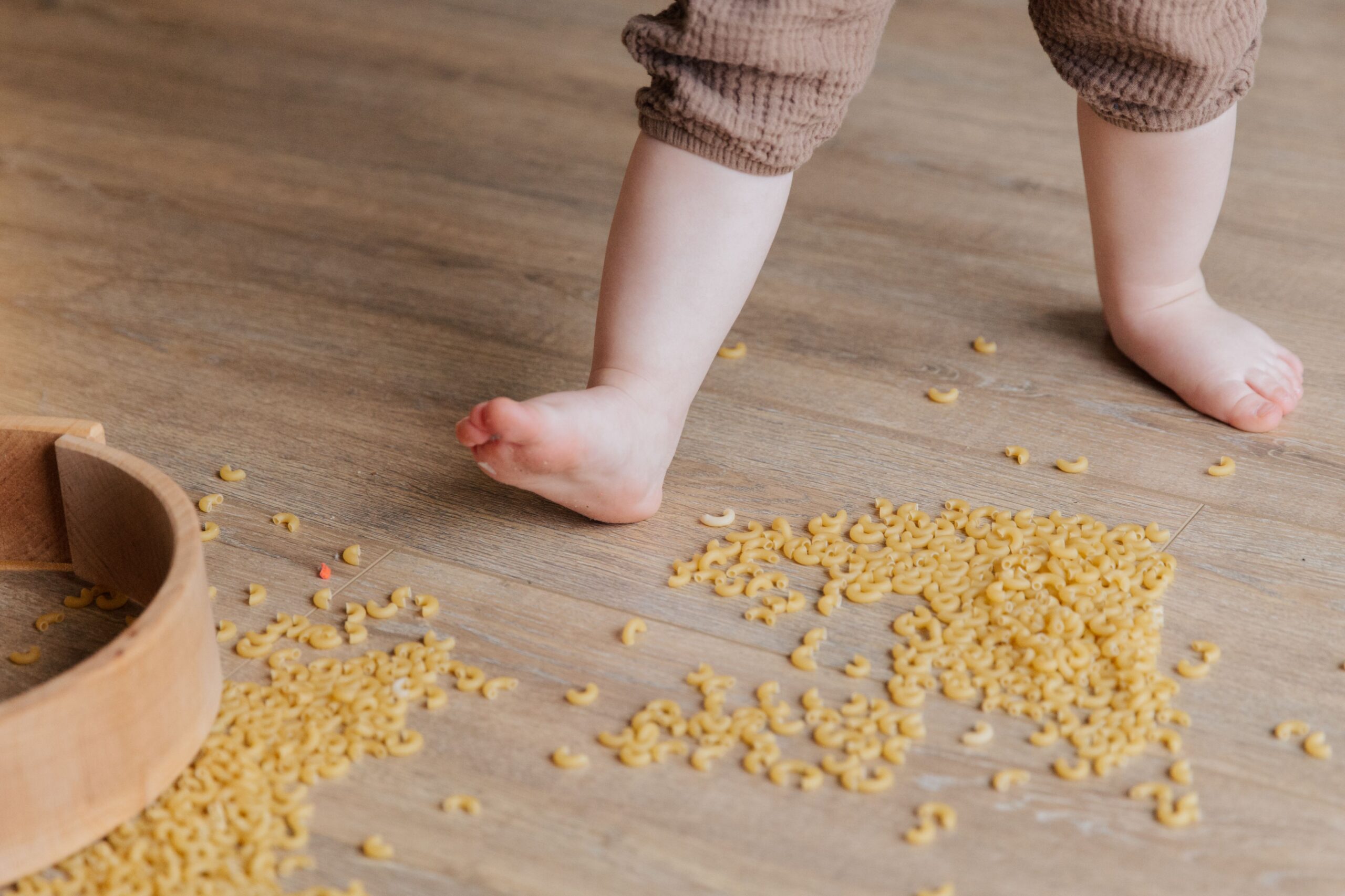 Toddler exploring textures with a macaroni sensory bin on the floor