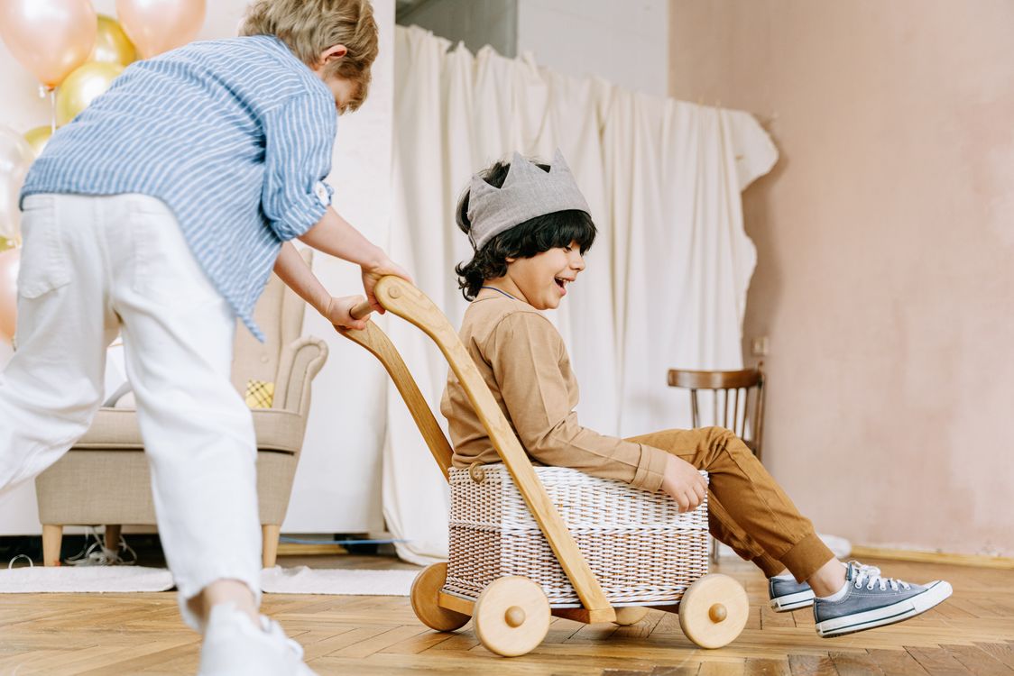 two young children playing with a wooden push walker toy, the same style of toy featured in this toys for 18 month old guide