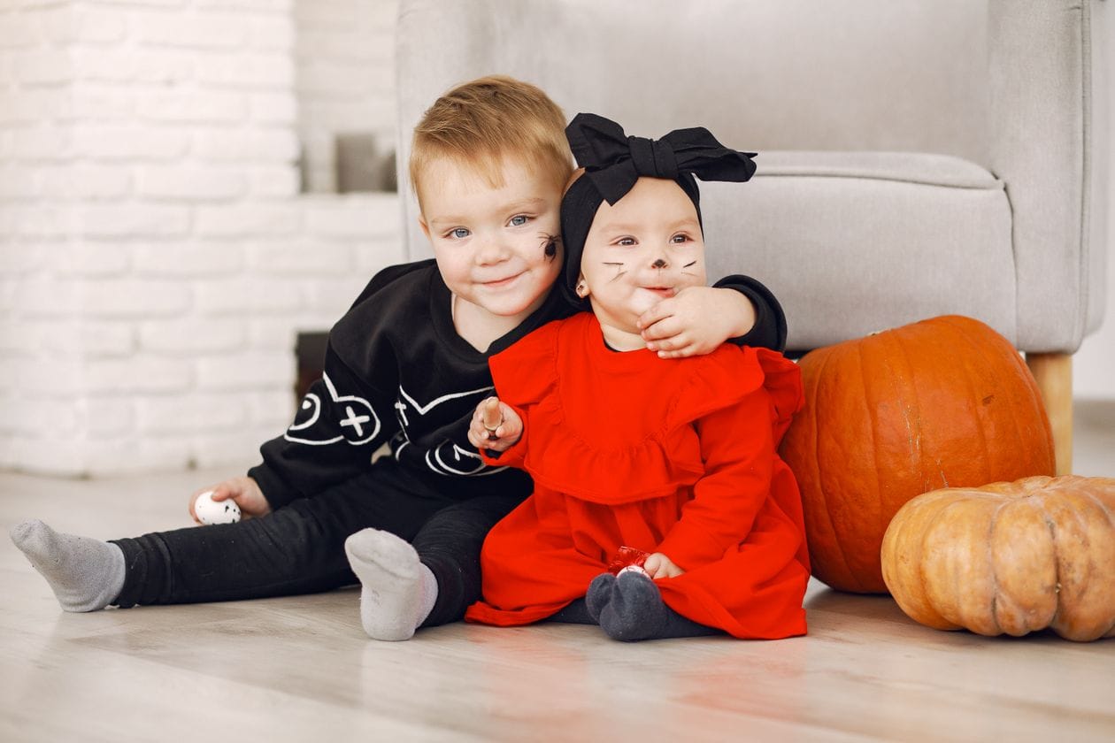 Two toddlers in halloween costumes sitting with pumpkins, a calm daycare-style setup for daycare halloween activities for toddlers