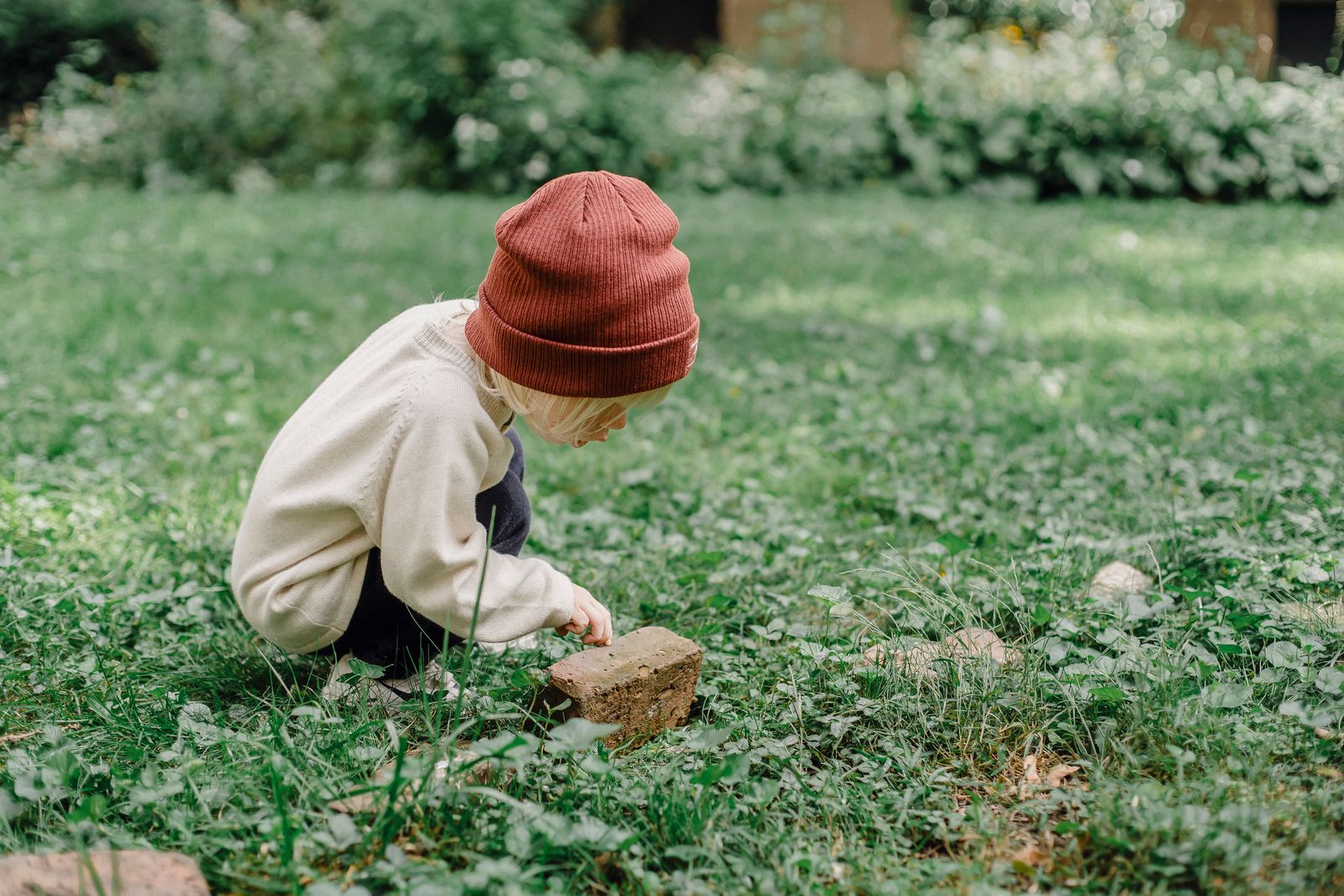 Toddler crouched down examining something in the grass, part of a nature scavenger hunt outdoor activity for toddlers