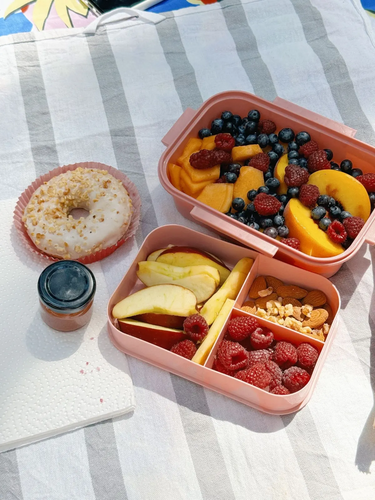 A divided bento-style lunch box with fruit, a bagel, and other toddler lunch components
