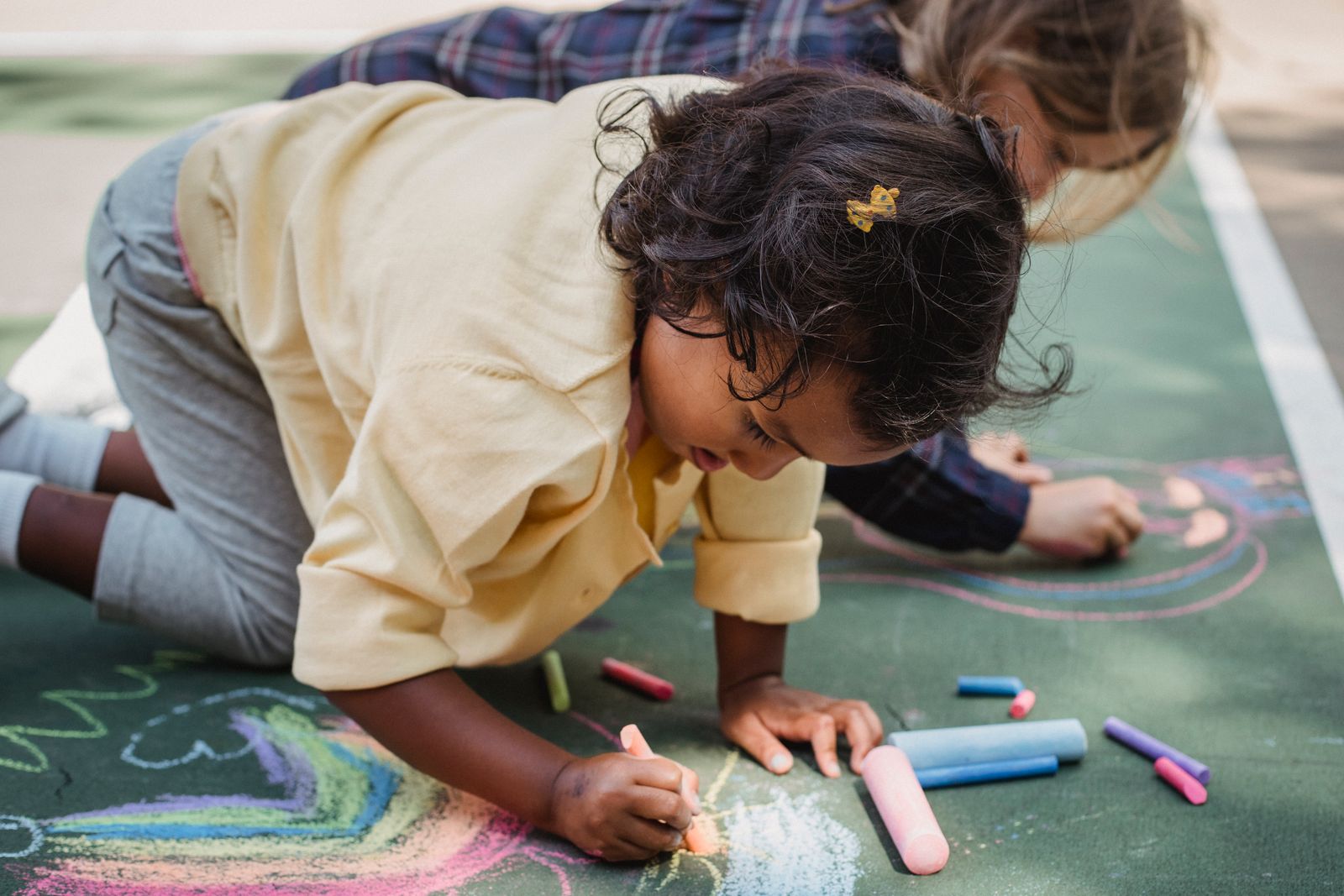 Toddlers drawing with sidewalk chalk on the pavement, part of a chalk hopscotch outdoor activity for toddlers